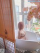 A naked woman sitting in a bathtub in front of a window.