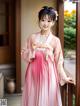 A woman in a pink hanbok standing on a balcony.