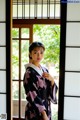 A woman in a kimono standing in front of a window.