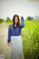 A woman in a blue shirt and white skirt standing on a dirt road.