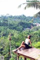 A woman sitting on a wooden platform in the middle of a lush green forest.