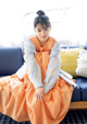 A woman sitting on a blue couch wearing an orange dress.