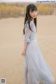 A woman in a long dress standing in the sand.