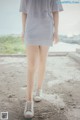 A woman in a gray dress is walking on a dirt road.