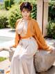 A woman in a kimono sitting on a rock by a pool.