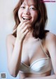 A woman in a white bra smiling and holding her hand to her mouth.