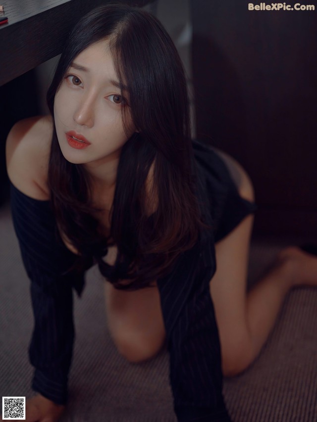 A woman in a black dress sitting on the floor.